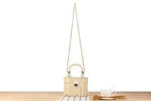 Detail of a beige straw woven bag with a gold metal chain strap on a wooden desk