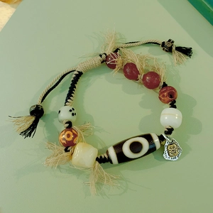 Close-up of handmade ethnic bracelet with Dzi bead, yak bone beads and metal face pendant