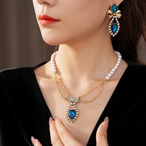 Close-up of pearl necklace and bow earrings with blue teardrop gemstone pendants