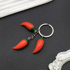 Realistic red resin chili pepper keychain with silver ring on black leather background