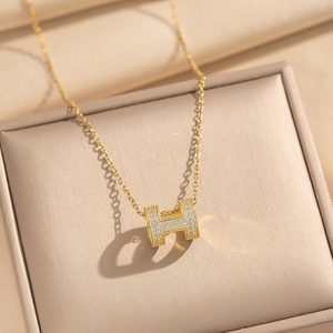 Collier élégant doré avec pendentif en H serti de zircons blancs sur boîte à bijoux