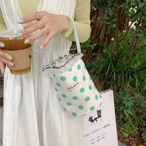 Close-up of white canvas mini handbag with green polka dots and wavy black lace trim decoration