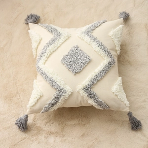 Close-up of tufted grey diamond geometric pattern and corner tassels on a beige cushion cover