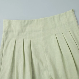 Detail view of high-waist pleated shorts in light green cotton linen with side zipper