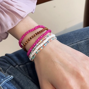 Detail of seven Bohemian beaded bracelets set in magenta, gold and white on woman's wrist