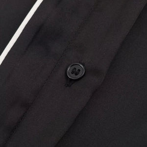 Detail of black satin shirt featuring contrast white piping and tonal four-hole button