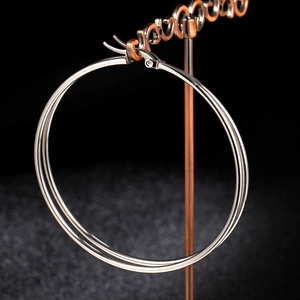 Close-up of polished silver titanium steel hoop earrings on a black display stand