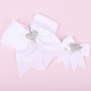 Close-up of two white grosgrain ribbon bows with silver sequin heart center on pink background