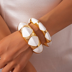 Detail of chunky gold enamel cuff bracelets with geometric wave pattern on a model's wrist
