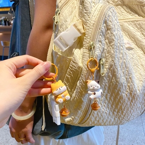 Cute resin magnetic cat couple keychain with bells on a textured beige backpack