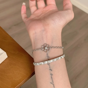 Détail d'un bracelet perle à fleur évidée et d'un jonc fleuri avec marguerites jaunes