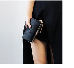 Close-up of black satin evening clutch with woven texture and gold tassel charm detail