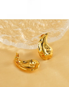 Macro shot of gold teardrop earrings with a hammered texture on smooth yellow satin