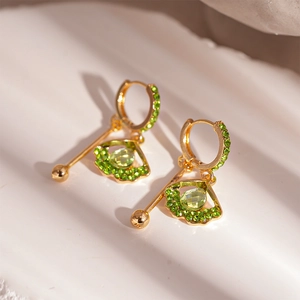 Detailed close-up of golden leaf earrings with emerald green rhinestones and faceted gems