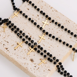 Minimalist black glass bead necklaces with gold cross pendants on beige stone display