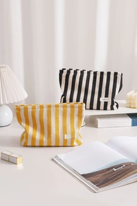 Detail of yellow and black striped canvas makeup bags on a white desk with props