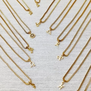 Detailed flat lay of golden box chain necklaces with twelve zodiac signs on fabric