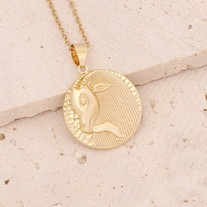 Macro detail of Aries zodiac gold pendant on textured stone background with chain