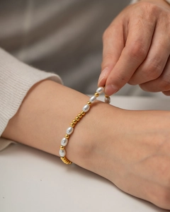 Vergoldetes Edelstahlarmband mit weißen Perlen und Metallperlen an einem Handgelenk