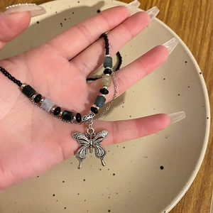 Detail of silver hollow butterfly pendant on beaded necklace with dark green accents