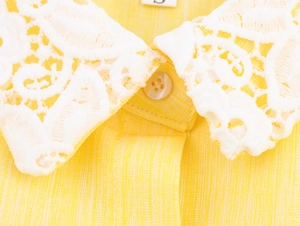 Detailed close-up of yellow linen dress featuring white lace embroidery and pearl button