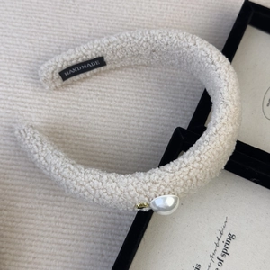 Detail of cream faux shearling headband with pearl accent and handmade label