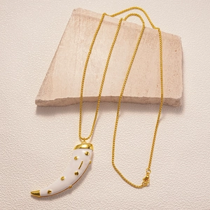 Detail of a white enamel horn pendant with golden dot accents on a gold chain necklace