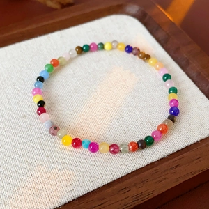 Close-up of colorful beaded bracelet on white linen fabric within a dark wooden tray