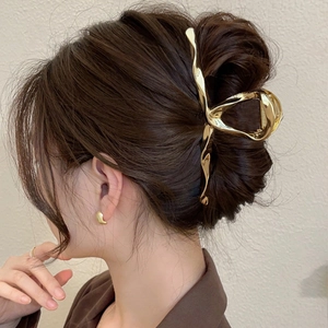 Macro detail of large gold metal hair claw clip holding hair in a chic bun style