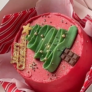 Close-up of a red Christmas mini cake with green frosting tree and gold Merry Christmas topper