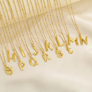 Close-up of golden alphabet pendants H to T on white silk background for jewelry