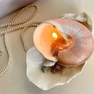 Close-up of a lit pink shell scented candle with decorative pearls and ocean shells