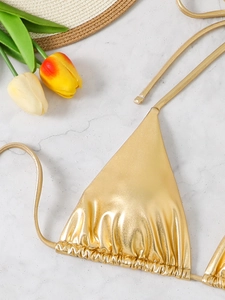 Detail of metallic gold triangle bikini top with ruched texture on marble background