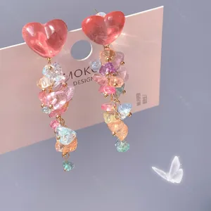 Détail de boucles d'oreilles pendantes avec cœurs en résine rose et perles de pierre colorées