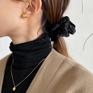 Detail of golden double hoop earrings and leaf pendant necklace worn with a black scrunchie