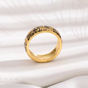 Detailed macro of gold ring featuring black enamel inlay and engraved leaf patterns
