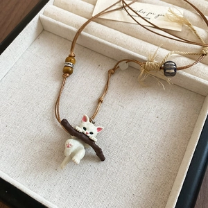 Detailed shot of a cute white cat pendant with wooden branch and beads on a woven rope