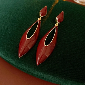 Detailed shot of dark red enamel drop earrings with gold edges on green velvet