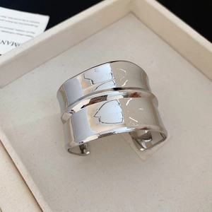 Bracelet jonc géométrique argenté poli présenté sur un plateau minimaliste beige