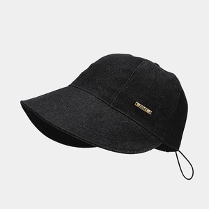 Detail of black denim sun hat with golden metal logo plate and adjustable wind cord