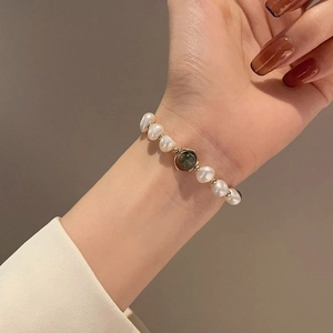 Detailed shot of a freshwater pearl bracelet with a green gemstone on a model wrist