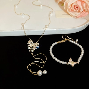 Detail of 18k gold butterfly necklace and pearl bracelet set on a floral display