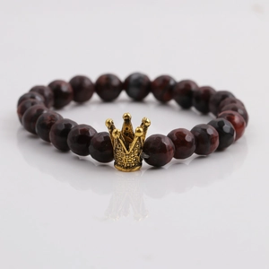 Detail eines dunkelroten facettierten Perlenarmbandes mit goldenem Kronenanhänger