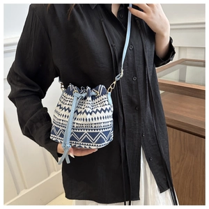Detail of small woven bucket bag with blue and white geometric patterns and crossbody strap
