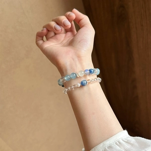 Detailansicht eleganter Armbänder aus weißem Kristall und blauen Perlen am Handgelenk