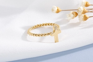 Detailed shot of golden twisted rope ring featuring a matte textured cross pendant charm