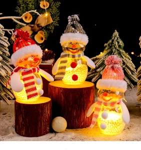 Three glowing Christmas snowmen in knit hats and scarves on wooden base with warm lights