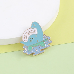Detail of blue dinosaur enamel pin showing the Believe in Yourself text and gold plating