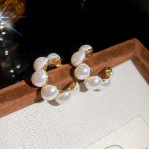 Macro shot of gold-plated C-shaped pearl stud earrings with vintage french design style