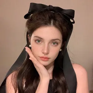 Detailed view of an oversized black fabric bow hair clip with long ribbons on a model